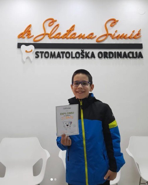Dečak sa diplomom za hrabrost ispred logotipa ordinacije