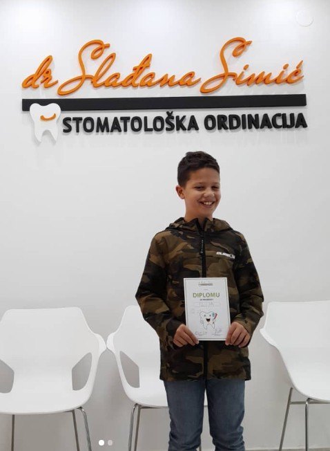 Dečak sa diplomom za hrabrost ispred logotipa ordinacije